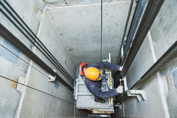 lift machinist worker adjusting elevator mechanism with spanners in elevator shaft hoistway